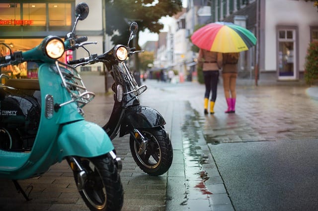 Geparkeerde scooters in een winkelstraat op een regenachtige dag, symbool voor de populariteit van scooters onder jongeren.