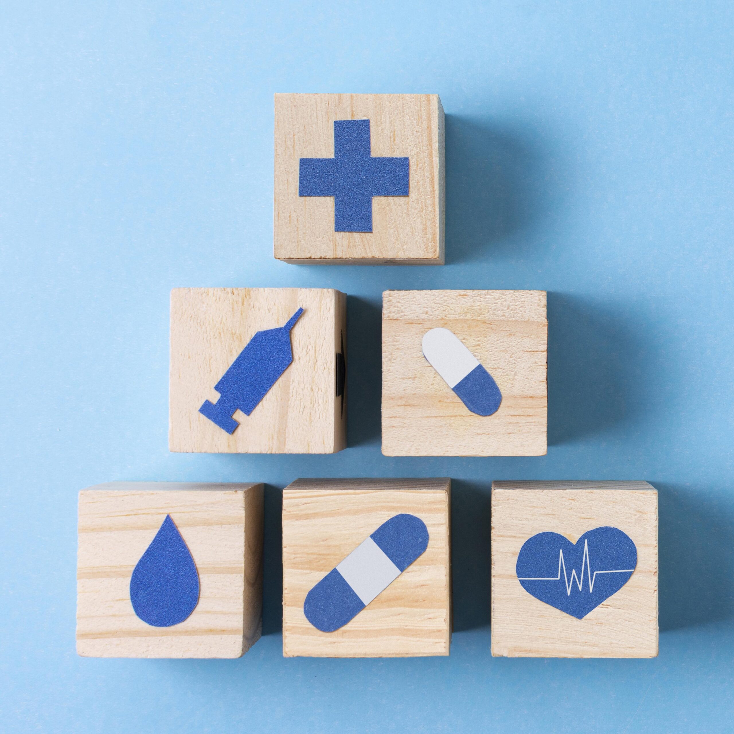 Houten blokjes met zorgsymbolen zoals een kruis, hart en medicatie op een blauwe achtergrond.