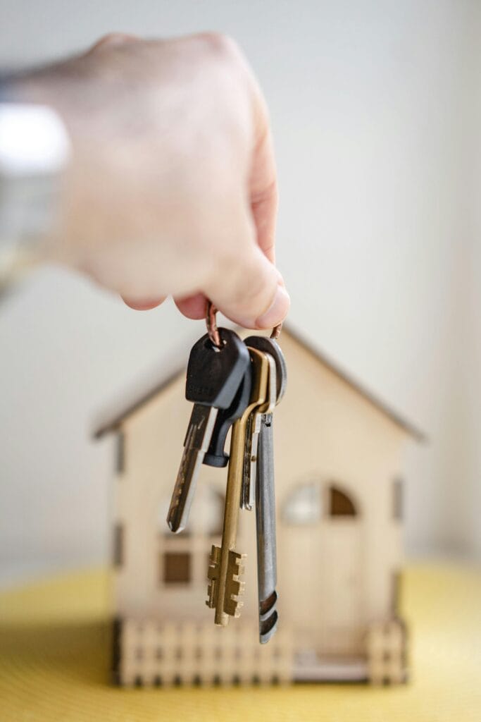 Huissleutels bij aankoop woning Hand met huissleutels voor een miniatuurwoning als symbool voor hypotheek en woningkoop.